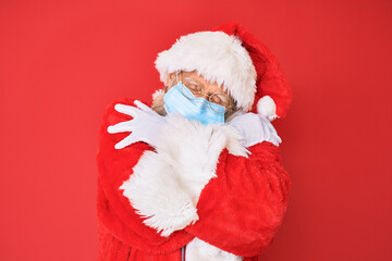 Old senior man wearing santa claus costume wearing safety mask hugging oneself happy and positive, smiling confident. self love and self care