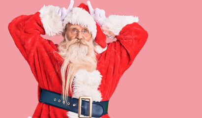 Old senior man with grey hair and long beard wearing traditional santa claus costume doing funny...