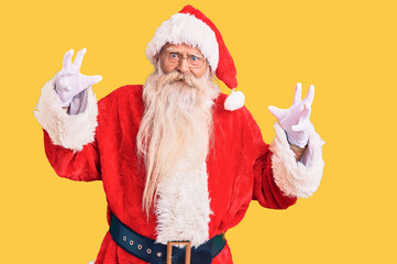Old senior man with grey hair and long beard wearing traditional santa claus costume shouting frustrated with rage, hands trying to strangle, yelling mad