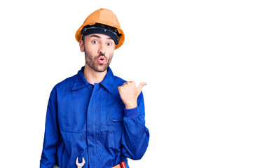 Young hispanic man wearing worker uniform surprised pointing with hand finger to the side, open mouth amazed expression.