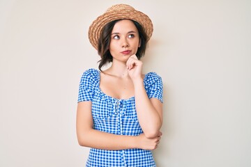 Young beautiful girl wearing summer hat thinking concentrated about doubt with finger on chin and...