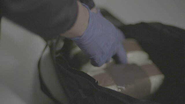 Police officer with blue gloves on opens bag containing cocaine parcels