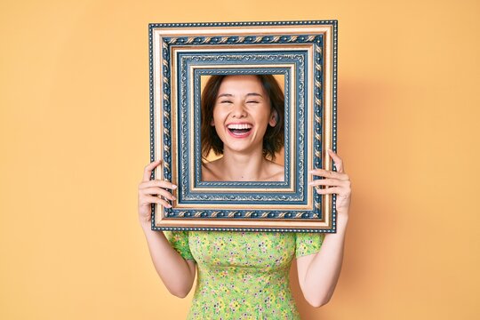 Young beautiful woman holding empty frame smiling and laughing hard out loud because funny crazy joke.