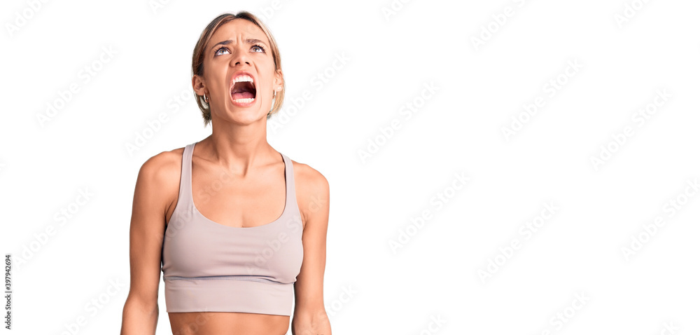 Wall mural beautiful caucasian woman wearing sportswear angry and mad screaming frustrated and furious, shoutin