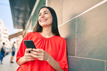 Young latin girl smiling happy using smartphone at the city.