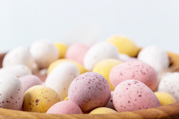 Close up Easter eggs in wooden bowl on blue background. Selective focus. Close-up. White yellow pink eggs for Easter treat.