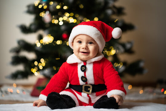 adorable little baby boy in a santa costume sitting on a soft fake fur in front of a christmas tree
