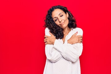 Middle age beautiful woman wearing casual shirt hugging oneself happy and positive, smiling...