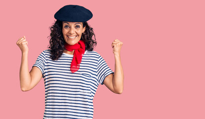 Middle age beautiful woman wearing french beret and scarf screaming proud, celebrating victory and success very excited with raised arms