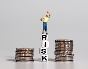 Miniature man standing on the white cubes with RISK word between piles of coins. Risk management...
