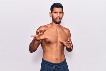 Young latin man standing shirtless disgusted expression, displeased and fearful doing disgust face...
