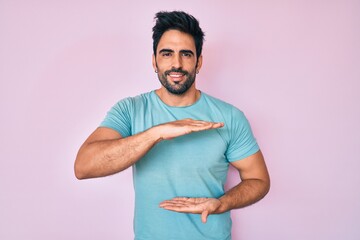 Handsome hispanic man with beard wearing casual clothes gesturing with hands showing big and large size sign, measure symbol. smiling looking at the camera. measuring concept.
