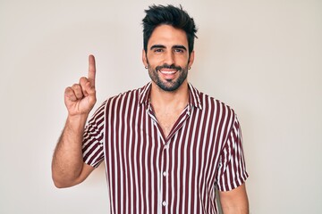 Naklejka premium Handsome hispanic man with beard wearing casual clothes pointing finger up with successful idea. exited and happy. number one.