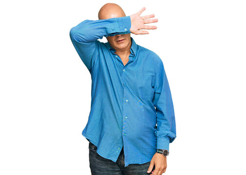 Middle age bald man wearing casual clothes covering eyes with arm, looking serious and sad. sightless, hiding and rejection concept