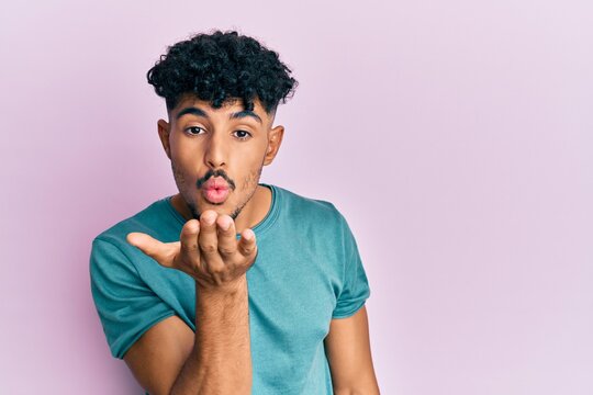 Young arab handsome man wearing casual clothes looking at the camera blowing a kiss with hand on air being lovely and sexy. love expression.