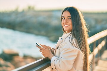 Young hispanic girl smiling happy using smartphone leaning on the balustrade.