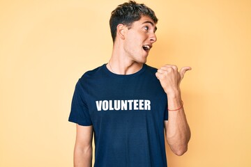 Young handsome man wearing volunteer t shirt pointing thumb up to the side smiling happy with open mouth