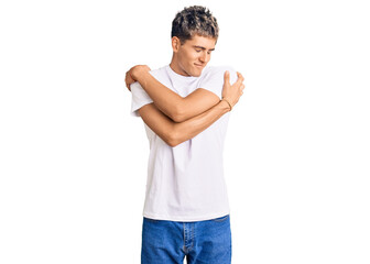 Young handsome man wearing casual white tshirt hugging oneself happy and positive, smiling...