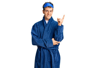 Young handsome man wearing sleep mask and bathrobe smiling happy pointing with hand and finger to the side