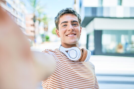 Young handsome caucasian man smiling happy wearing headphones making selfie by the camera walking at city.