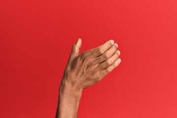 Hand of hispanic man over red isolated background holding invisible object, empty hand doing...