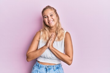 Young blonde girl wearing casual clothes praying with hands together asking for forgiveness smiling confident.