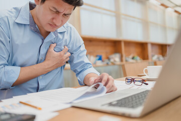 Businessman holding his heart in pain, heart attack, chest pain between working.