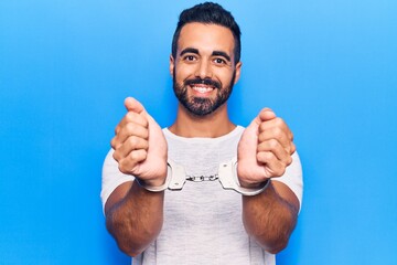 Young hispanic man wearing prisoner handcuffs looking positive and happy standing and smiling with...