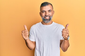 Middle age handsome man wearing casual white tshirt success sign doing positive gesture with hand, thumbs up smiling and happy. cheerful expression and winner gesture.