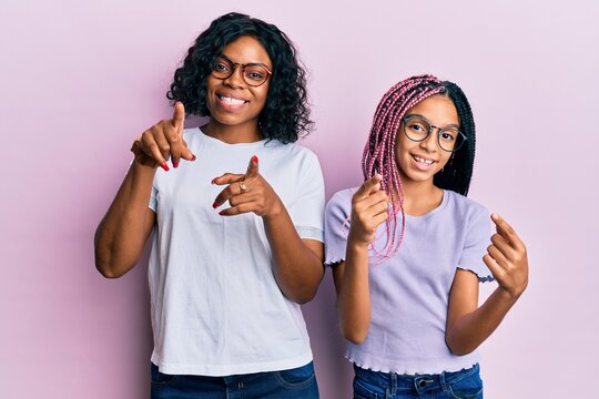 Beautiful african american mother and daughter wearing casual clothes and glasses pointing fingers to camera with happy and funny face. good energy and vibes.