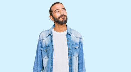 Attractive man with long hair and beard wearing casual denim jacket smiling looking to the side and staring away thinking.