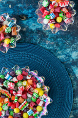 Top down view of vintage glass dishes filled with Christmas candy, against a blue background.
