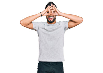 Fototapeta na wymiar Young man with beard wearing casual grey tshirt doing ok gesture like binoculars sticking tongue out, eyes looking through fingers. crazy expression.