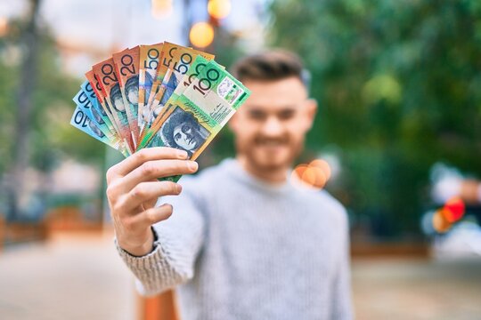 Young caucasian man smiling happy holding australian dollars at the park.