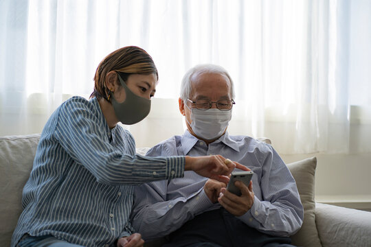 マスクをつけてスマートフォンを見る日本人シニア男性と娘