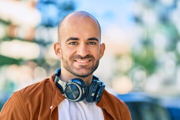 Young hispanic bald man smiling happy using headphones at the city