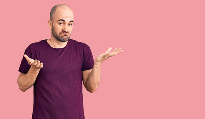 Young handsome man wearing casual t shirt clueless and confused expression with arms and hands...