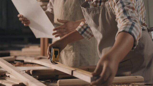 Midsection footage of unrecognizable man with little boy wearing aprons working with wood measuring slats with tape-line making diy deck chair