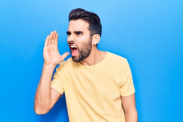 Fototapeta premium Young handsome man with beard wearing casual t-shirt shouting and screaming loud to side with hand on mouth. communication concept.