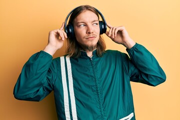 Handsome caucasian man with long hair wearing gym clothes and using headphones smiling looking to the side and staring away thinking.