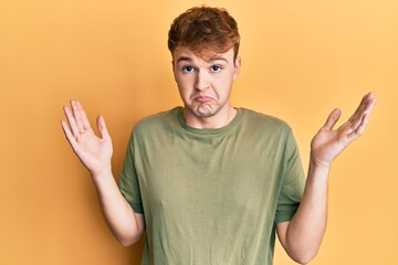 Naklejka premium Young caucasian man wearing casual green t shirt clueless and confused with open arms, no idea and doubtful face.