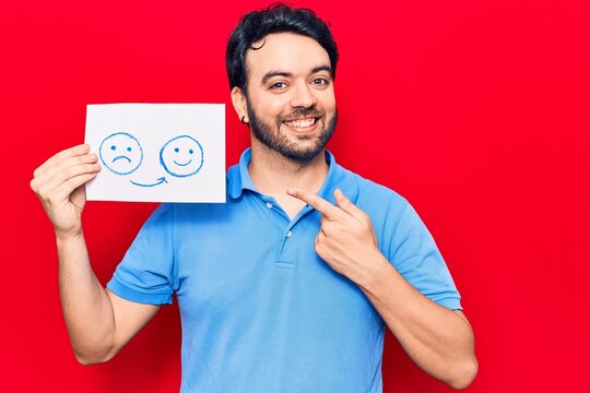 Young hispanic man holding sad to happy emotion paper smiling happy pointing with hand and finger