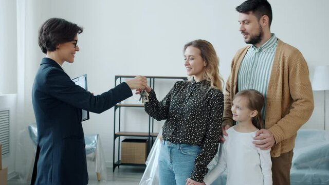 Young woman is making deal with realtor taking key shaking hands hugging husband and daughter standing inside beautiful apartment. Business and housing concept.