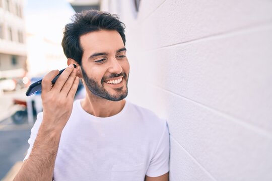 Young hispanic man smiling happy listening audio message using smartphone at city.