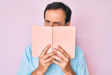 Middle age hispanic man reading book skeptic and nervous, frowning upset because of problem....