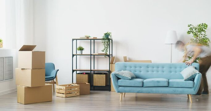 Time-lapse of young couple man and woman bringing boxes and furniture to empty house relocating decorating interior then relaxing on couch together.