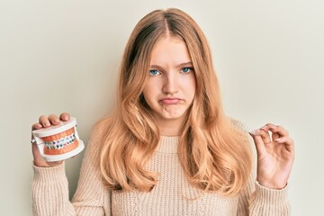 Beautiful young caucasian girl holding invisible aligner orthodontic and braces depressed and worry...