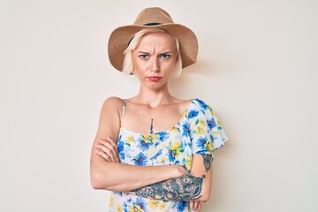 Young blonde woman with tattoo wearing summer hat skeptic and nervous, disapproving expression on face with crossed arms. negative person.