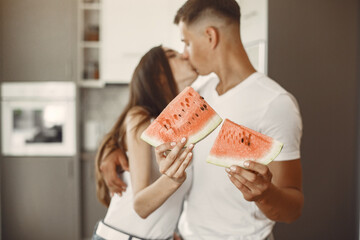 Cute couple in a kitchen. Lady in a white t-shirt. Pair at home eating watermelon.