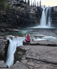 Woman meditating on cliff by Crescent Falls in Alberta. Norgedd. Canada.